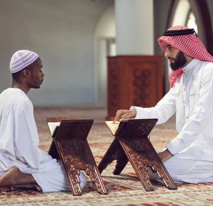 Two men in a mosque, one raising his index finger while reciting the Shahada